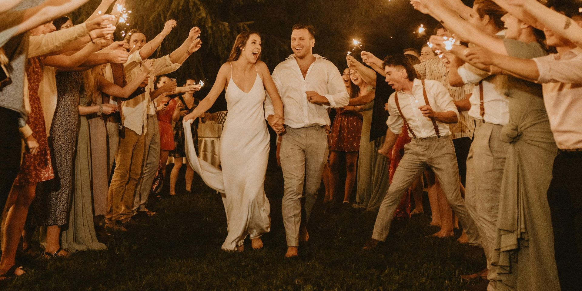 Bride and groom joyfully exit surrounded by sparkling celebratory guests at a nighttime wedding.
